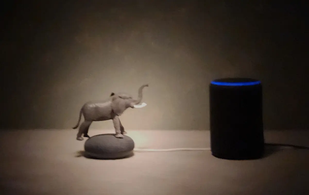 Ancient Wisdom Listening Small elephant figurine placed on a smart speaker with another speaker beside it, photographed in soft directional light.