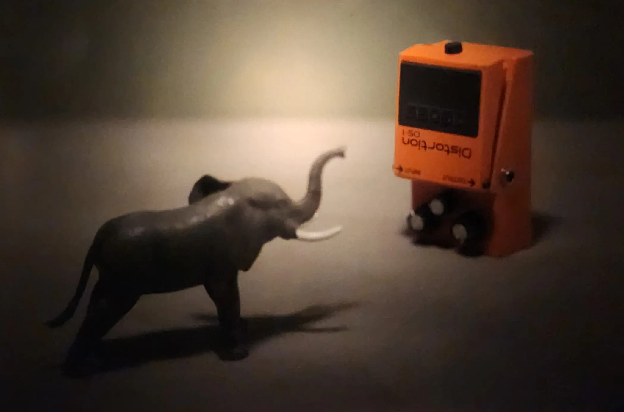 Elephant vs. DS‑1 — The Noise Small elephant figurine positioned beside an upside‑down DS‑1 distortion pedal, photographed in soft directional light