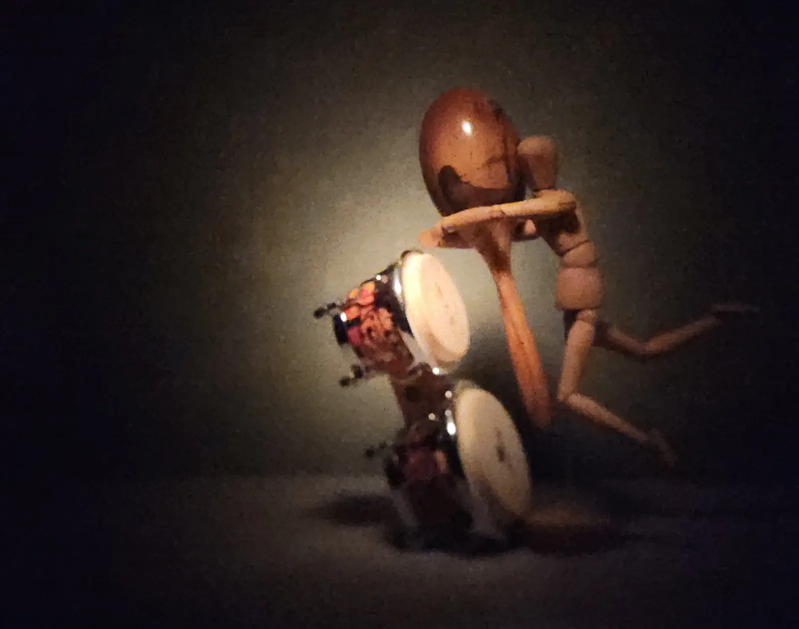 The Joy of Motion Wooden artist mannequin posed as if playing a pair of bongo drums under focused studio lighting.